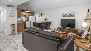 A modern living room with a sofa, a TV, and a dining area with a kitchen in the background. - Updated condo with pools near golf courses (St. George)