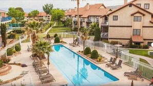 A swimming pool surrounded by lounge chairs and palm trees, with a view of apartment buildings in the background. - Updated condo with pools near golf courses (St. George)