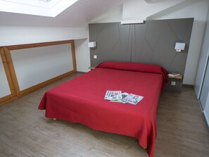 A bedroom with a red bedspread, wooden floor, and a skylight.