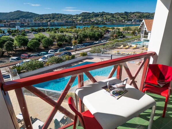 A balcony with a pool, red and white chairs, and a table with magazines.