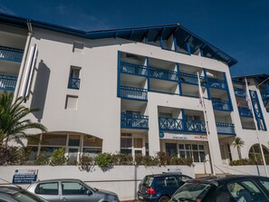 A multi-story building with balconies, a sign indicating it's a hotel, and parked cars in front.