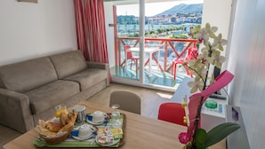 Une chambre meublée avec balcon, une table à manger avec des produits pour le petit-déjeuner, et une vue sur un paysage montagneux.