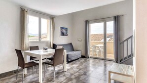 A modern living room with a dining area, large windows, and a balcony. - Piscine sur place ! Appart avec Climatisation (Latour-Bas-Elne)