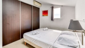 A bedroom with a bed, a wardrobe, a painting, a window, and a lamp. - Piscine sur place ! Appart avec Climatisation (Latour-Bas-Elne)