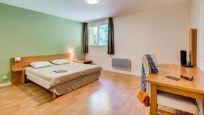 A bedroom with a bed, bedside table, lamp, window, radiator, and a desk with a chair. - Près des Pistes! Studio Charmant | Accès Sauna (La Féclaz)