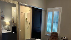 Una habitación de hotel con una cama grande, un espejo, un armario, una mesita y una ventana con persianas.