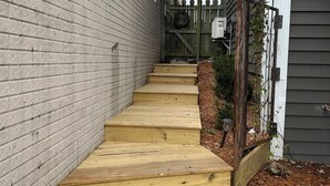 Una escalera de madera que conduce a una casa, con un muro de ladrillo a un lado y una cerca de madera al otro.