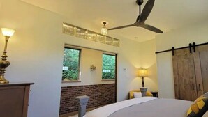 Una camera da letto con un letto, una ventola a soffitto, una finestra, un muro in mattoni, una porta di legno e una lampada.