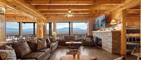 Interior de madera con chimenea, zona de estar y ventanas amplias que ofrecen vistas a la montaña.