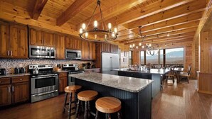 A spacious kitchen with wooden cabinets, stainless steel appliances, and a large island with stools. - Luxury Cabin Awesome Mountain Views Sleeps 42 (Sevierville)