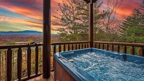 A hot tub on a wooden deck with a view of a sunset and mountains. - Luxury Cabin Awesome Mountain Views Sleeps 42 (Sevierville)