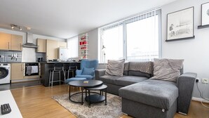 En modern lägenhet med kök, matplats och vardagsrum. Den har en grå soffa, en blå fåtölj och ett runt soffbord.