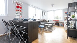 Ett modernt kök med en central köksö, matstolar, en soffa, ett soffbord och en bokhylla full med böcker.