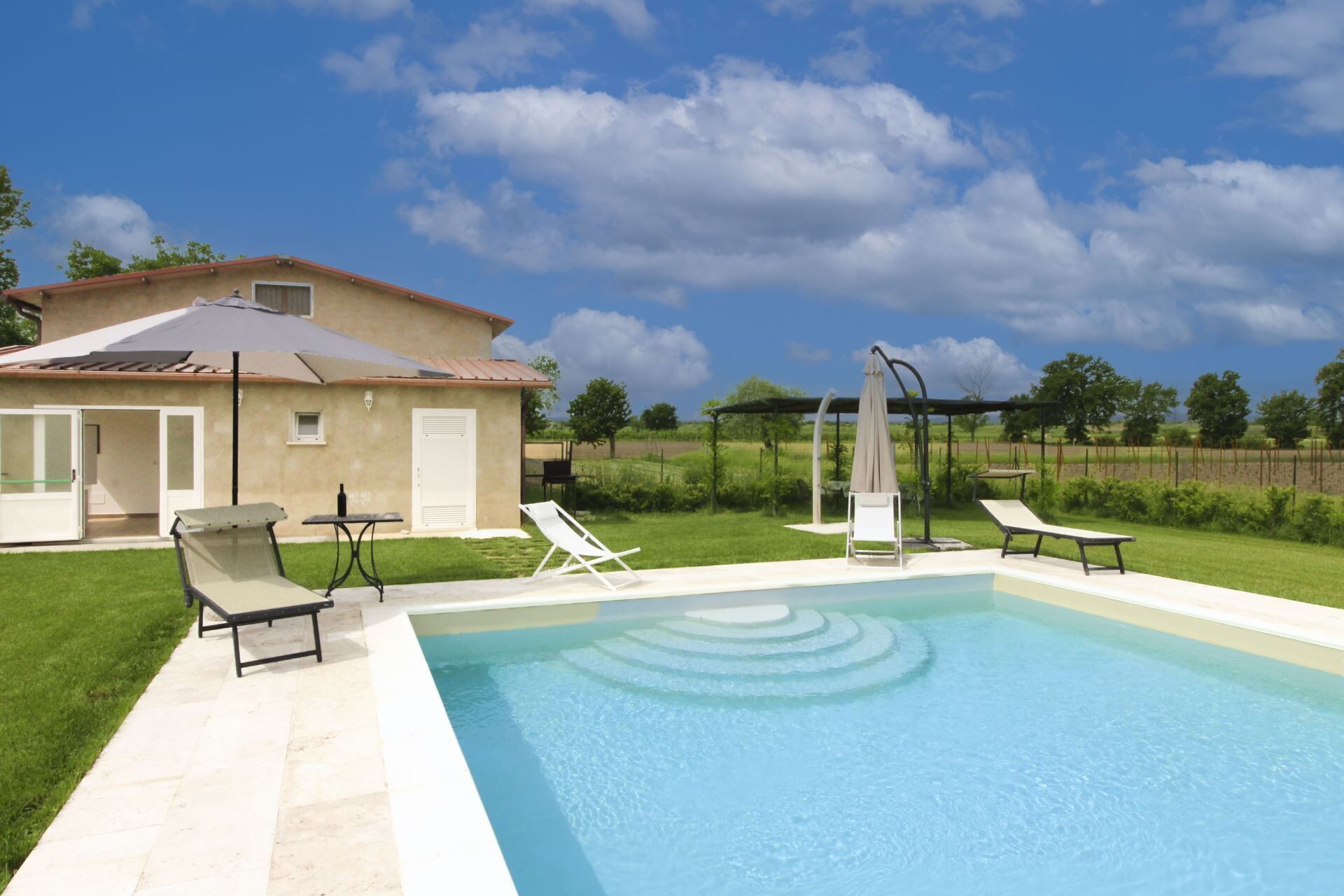 Piscina con sillas de descanso y una pérgola, rodeada de una casa y un césped.