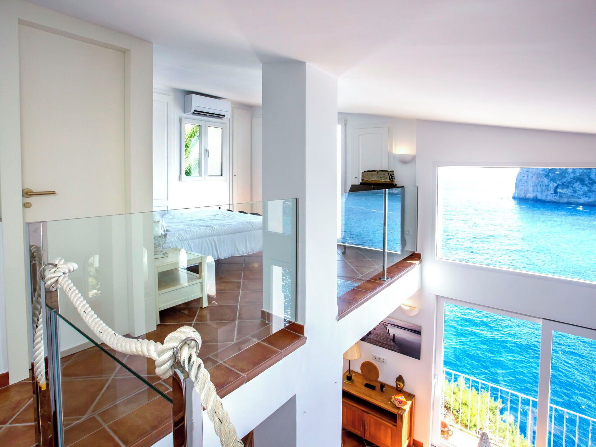A hotel room with a balcony, a bed, a desk, and a view of the sea.