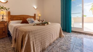 Un dormitorio con una cama de madera, una mesita de noche, una lámpara, una bandeja con vasos y vistas al exterior a través de una puerta corredera.
