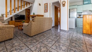 Una sala de estar con sofá, televisión, escalera de madera y un área de cocina.
