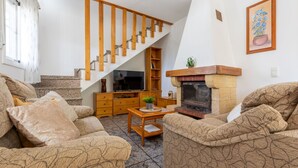 Una sala de estar con chimenea, escalera de madera y televisor.
