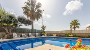Una piscina con sillones de descanso, palmeras y cielo despejado.