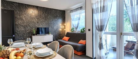 En moderne stue med spiseplads, et fjernsyn og en sofa med orange puder.