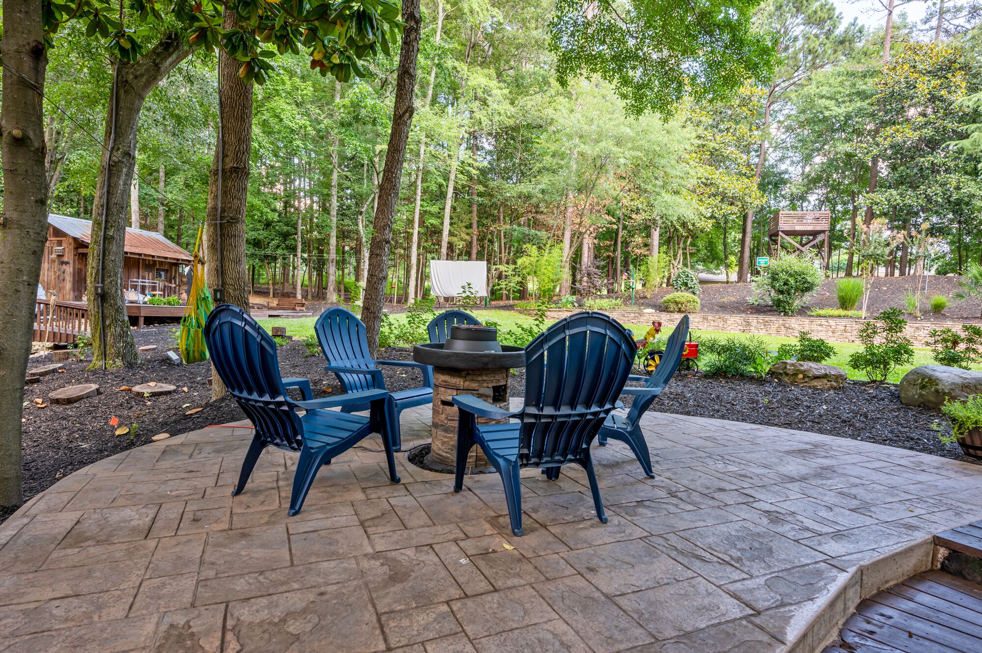 Une terrasse extérieure avec quatre fauteuils Adirondack, une table ronde et un foyer en pierre.