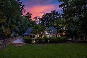 A house with a covered patio, surrounded by trees and a stone wall.