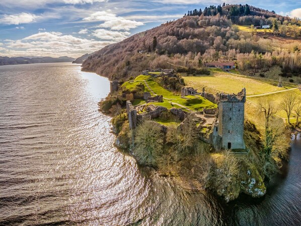 Eine historische Burgruine an einem See unter blauem Himmel.