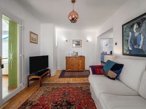 Una sala de estar con un sofá blanco, un televisor, un mueble de madera y un tapete rojo con estampado.