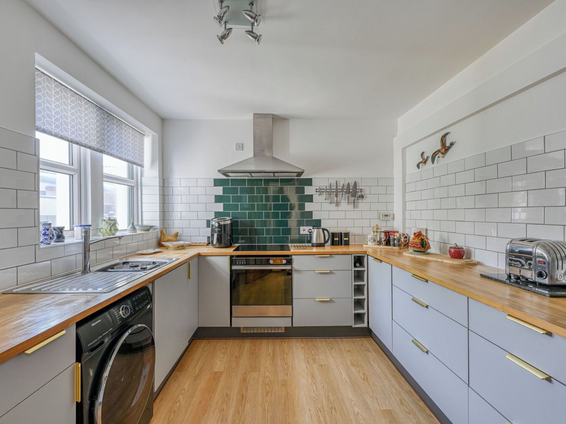 A modern kitchen with white cabinetry, a wooden countertop, a stainless steel range hood, and a dishwasher.