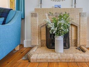 Una sala de estar con chimenea, un sillón azul y un jarrón blanco con flores.