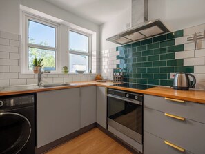 Cocina equipada con lavavajillas, horno y ventana con vistas a follaje.