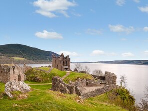 Eine historische Burgruine mit einem See im Hintergrund, umgeben von grasbewachsenen Hügeln.