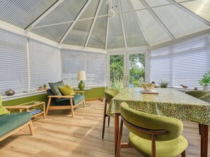 Un invernadero con techo de cristal, suelo de madera y mobiliario tapizado en verde.
