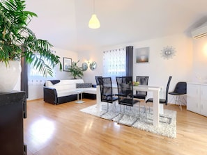 Een moderne woonkamer met een witte bank, zwarte stoelen, een eettafel en een grote potplant.