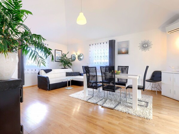 Uma sala de estar moderna com um sofá branco, cadeiras pretas, uma mesa de jantar e uma grande planta em vaso.