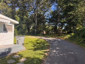 A gravel path leading to a small white cabin with a trash bin and a wooden deck.