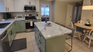 A modern kitchen with a central island, white cabinets, and a dining area with a table and chairs. - Classy Copacetic Cottage-King bd, Clean, close to Downtown, Furman, Swamp Rabbit (Greenville)