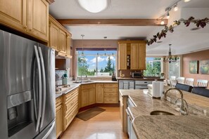 Une cuisine moderne avec des meubles en bois, des appareils en acier inoxydable, des comptoirs en granit et une grande fenêtre donnant sur la verdure.