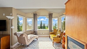 A spacious room with a large window, a television, a sofa, and a chair. - Hillside Haven (Anchorage)