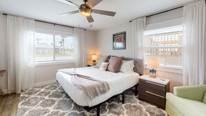 A bedroom with a bed, nightstands, a ceiling fan, and large windows with blinds. - First Floor Condo, Faces Shared Pool, Golf Cart Access (Port Aransas)