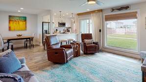 A modern living room with a sofa, chairs, a dining table, and a kitchen area with a large window. - First Floor Condo, Faces Shared Pool, Golf Cart Access (Port Aransas)