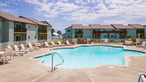 A swimming pool surrounded by lounge chairs and a building with multiple balconies. - First Floor Condo, Faces Shared Pool, Golf Cart Access (Port Aransas)