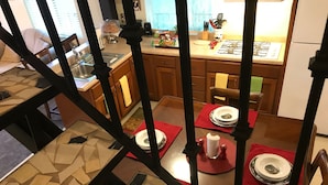 Un coin repas avec un sol carrelé, des chaises en bois et une table dressée pour deux personnes, agrémentée de sets de table rouges.