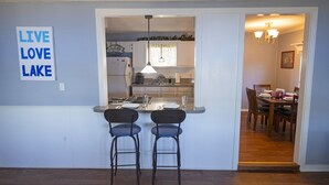 A compact kitchen with a bar area, two bar stools, and a dining table with chairs. - Lazy Days Lakefront Retreat Lake Granbury home, yard, dock-lift, covered parking (Granbury)