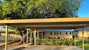 A covered outdoor area with a concrete floor, a tree, and a building in the background. - Lazy Days Lakefront Retreat Lake Granbury home, yard, dock-lift, covered parking (Granbury)