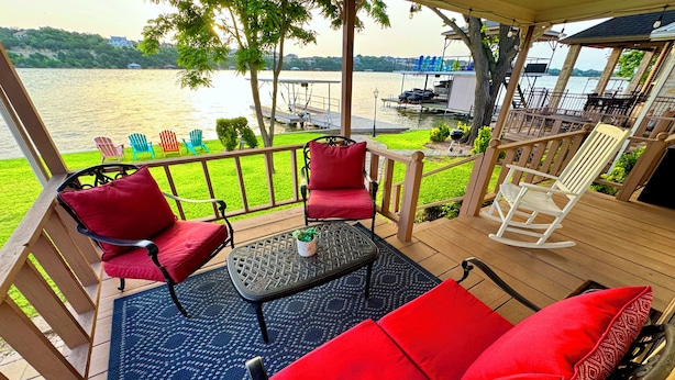 A covered outdoor seating area with red cushioned chairs and a table, overlooking a lake with a dock and boats. - Lazy Days Lakefront Retreat Lake Granbury home, yard, dock-lift, covered parking (Granbury)
