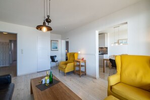 En moderne stue med et træbord, gule lænestole, et spisebord og et køkken i baggrunden.