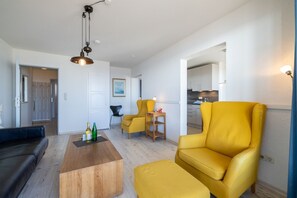 En moderne stue med et træbord, gule lænestole, en sort sofa og et køkken i baggrunden.