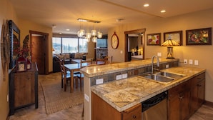 A spacious kitchen with granite countertops, a dishwasher, and a large island. There is a dining area with a table and chairs, and a living room with a sofa and a TV. - Purgatory Lodge 405 - Managed by Purgatory Resort (Durango)