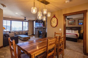 A spacious living area with a wooden dining table, comfortable seating, a stone fireplace, and a large wall clock.